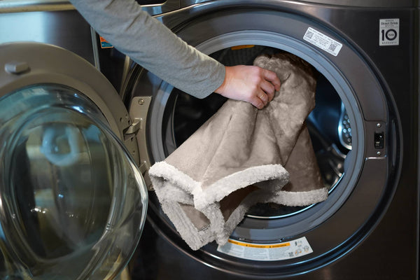 A brown and white sherpa dog bed cover being put into a washing machine at Furhaven Pet Products.